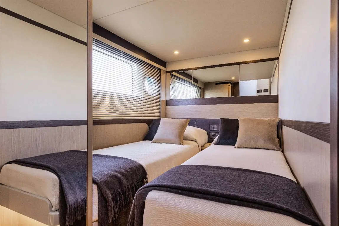 Modern twin bedroom with two beds, pillows, grey throws, window blinds, and mirrored wall reflecting bright interior.